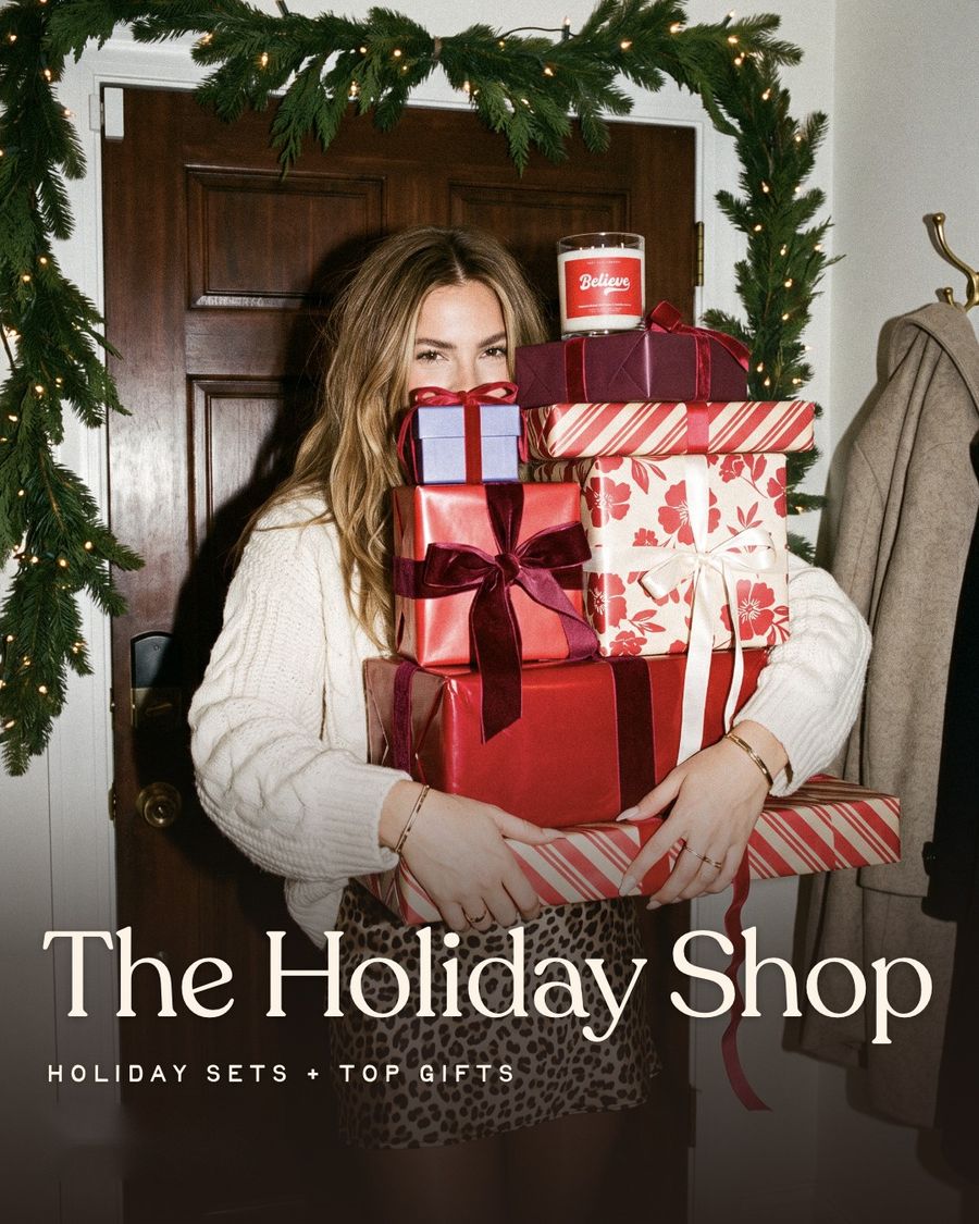 The Holiday Shop: holiday sets and top gifts. A woman holding a stack of wrapped gifts topped with the Believe candle.
